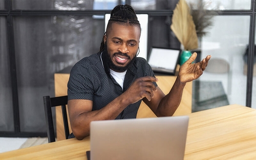 A man sitting at a table and having a conversation with someone via a computer.