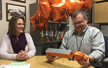 Todd Jadin holds a model Schneider semi-truck with orange 30th anniversary balloons floating behind him.