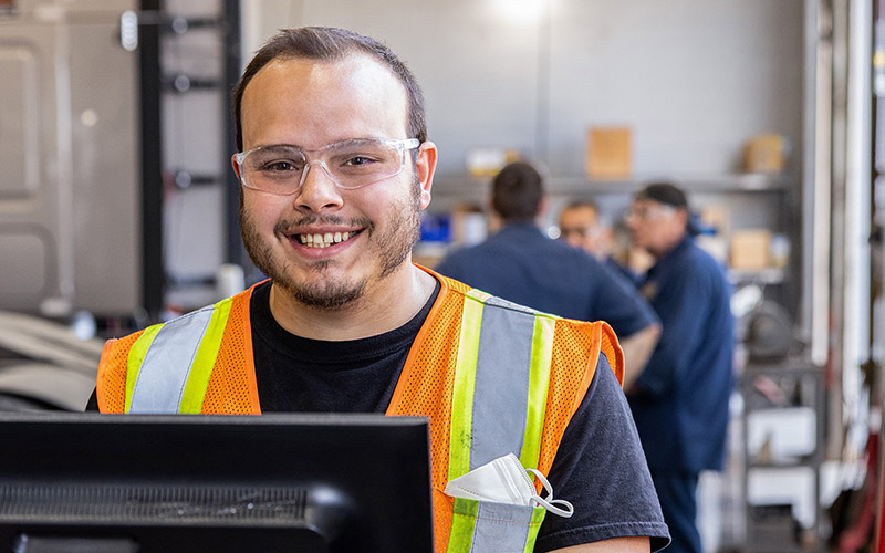 A Schneider diesel technician smiles while standing in front of a computer monitor in a shop.