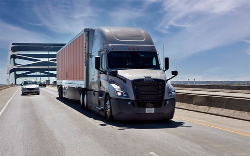 A Schneider semi-truck with a grey cab passing under a bridge on the highway.