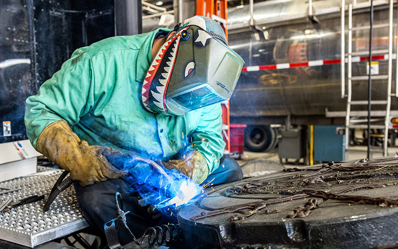 A man wearing a welding mask works in a shop.