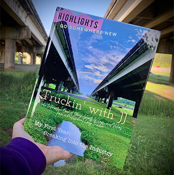 A hand holds JJ's book and on the cover of the book are two highways over a green marsh and a blue sky with white clouds.