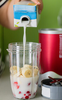 Someone pours milk into a personal blender containing strawberries and bananas.