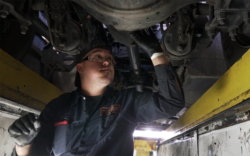 A Schneider diesel technician completes repairs to the underside of a Schneider truck.