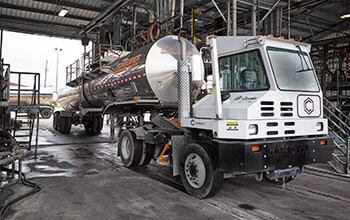 A white terminal tractor truck pulls a Tanker trailer into a shop.