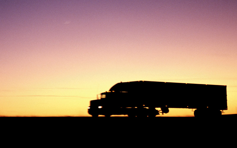 The silhouette of a semi-truck in front of a sunset.