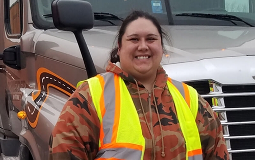 Schneider associate Kat Burt poses in front of a Schneider company truck while wearing a bright yellow safety vest.