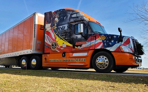 Jon’s Ride of Pride truck, which is custom wrapped with patriotic imagery and war photos, is parked at a grassy park. An evergreen wreath is attached to the grill of the truck.