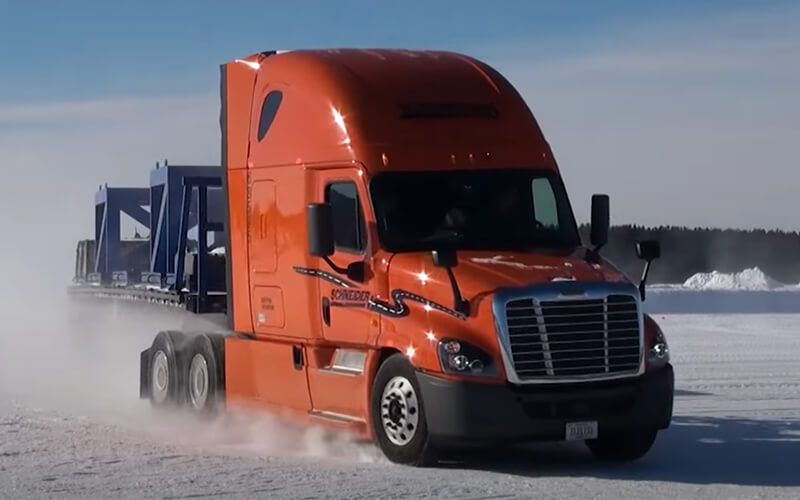 Schneider semi-truck kicks up dirt while hauling an intermodal trailer down the road