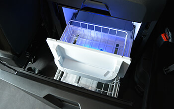 A built-in refrigerator is open and shows food storage space in a sleeper cab.