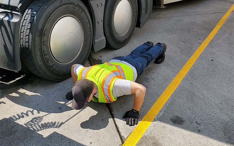 A truck driver does pushups on the pavement alongside his truck.