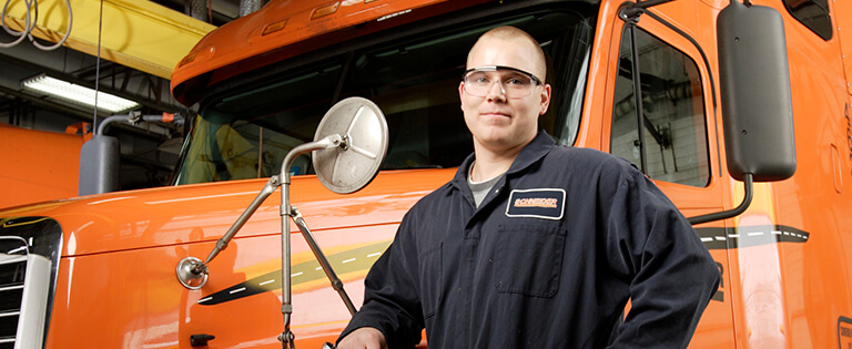 A Schneider diesel technician poses with his arm resting on a company truck