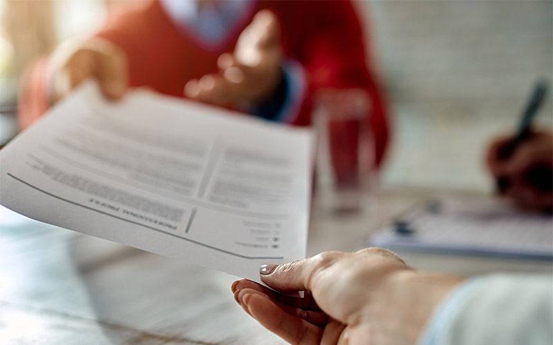 A resume being handed to someone across a table.