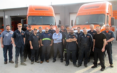 Schneider diesel technicians gather around two orange trucks outside of a company diesel shop