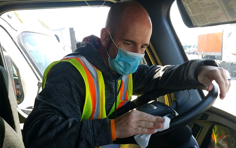 Truck driver with mask cleaning his truck.