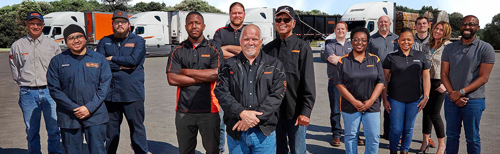 A group of 14 Schneider associates pose together in front of a row of company trucks
