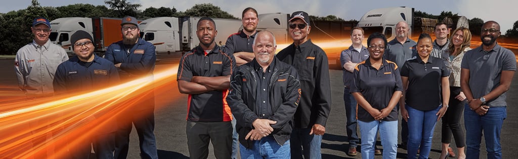 A group of 14 Schneider associates pose together in front of a row of company trucks