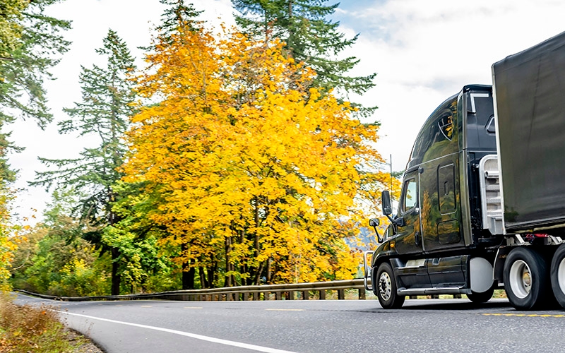 A semi-truck drives down a country road in fall.