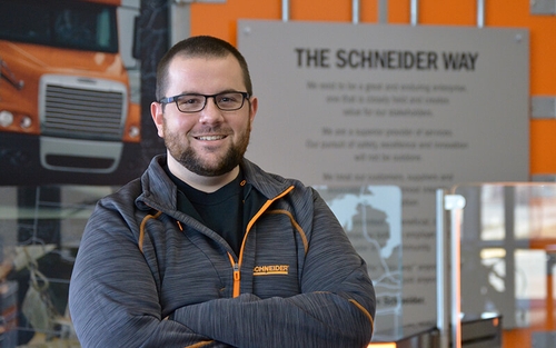 Andrew Becker, wearing a grey and orange Schneider quarter zip, poses with his arms crossed.