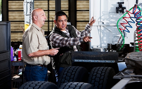 Two diesel technicians looking at the back of a semi tractor.