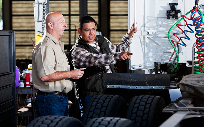 Two diesel technicians looking at the back of a semi tractor.