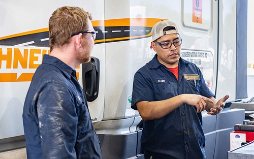 Two diesel technicians talking by a Schneider semi-truck