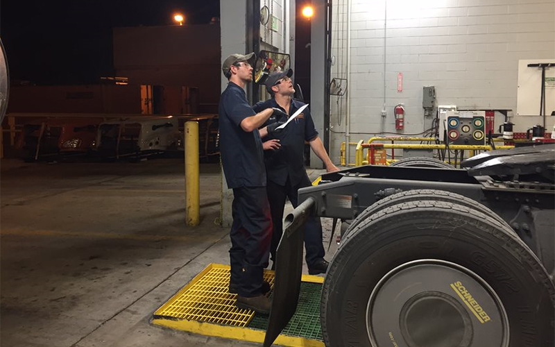 Two Schneider diesel technicians discuss repairs while standing at the back end of a tractor 