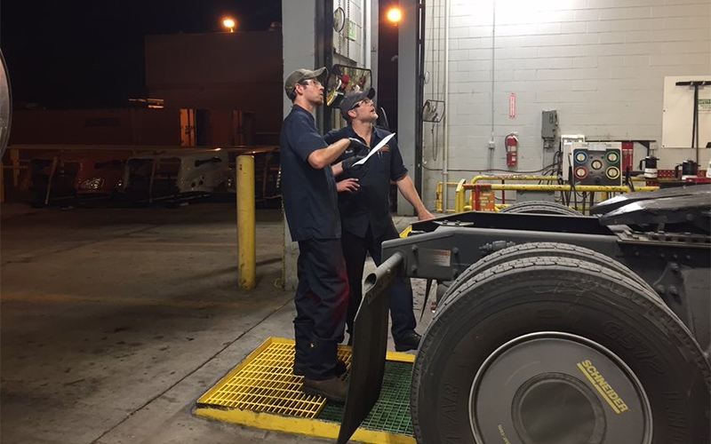 Two Schneider diesel technicians discuss repairs while standing at the back end of a tractor