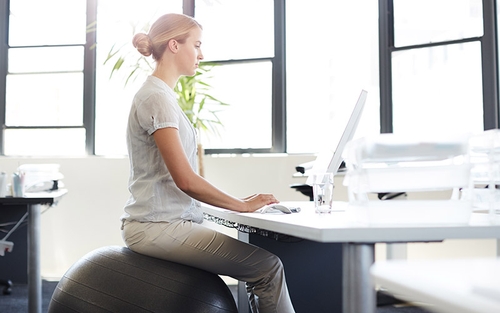 A woman sitting on a stability ball while working at her desk.