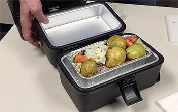 An open 12-volt portable stove contains cooked carrots, potatoes and beef.