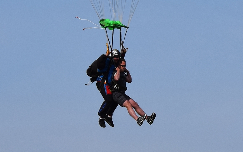 Josh kicks his legs outward while parachuting to the ground with his instructor.