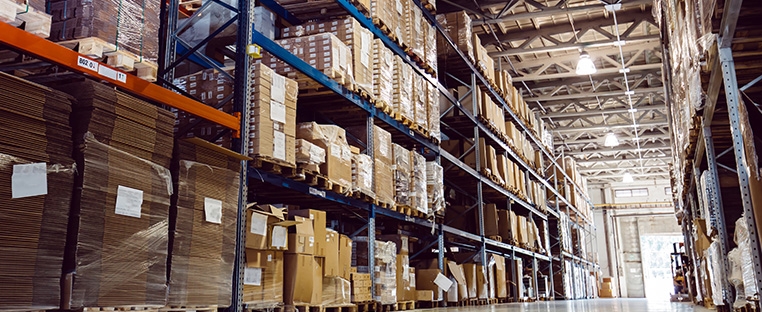 A floor level photo of tall shelves in a warehouse with pallets of boxes