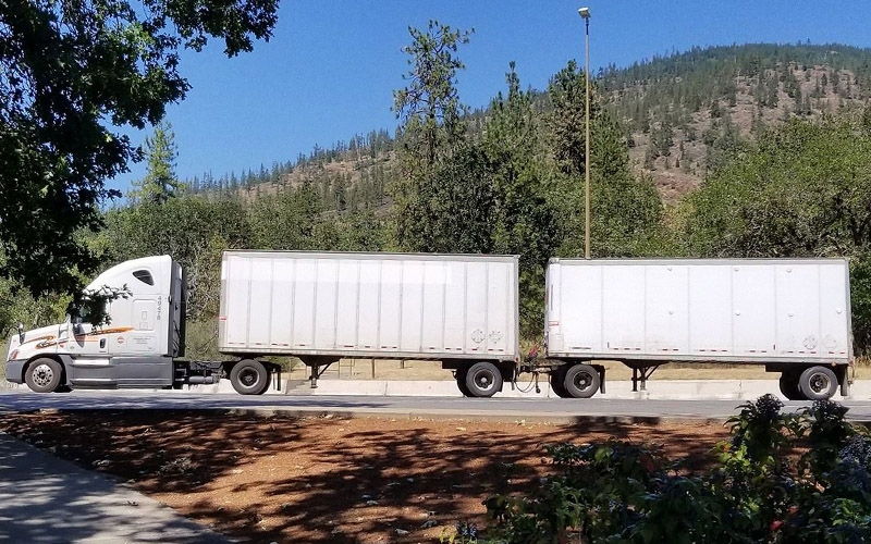 A white Schneider truck hauling double pup trailers in front of a large hill.