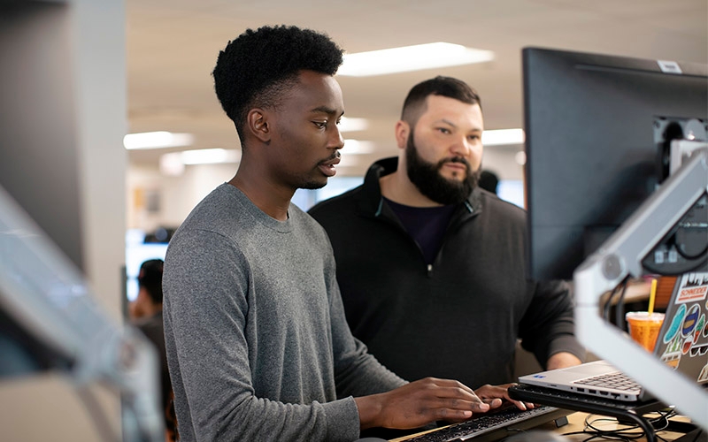 Two men standing up and looking at a computer screen.