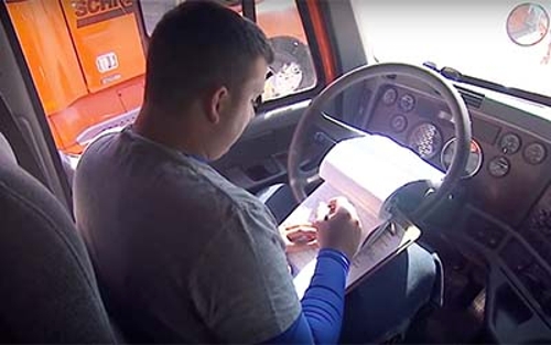 A Schneider driver sits in the driver seat while parked, jotting down information in a notepad.