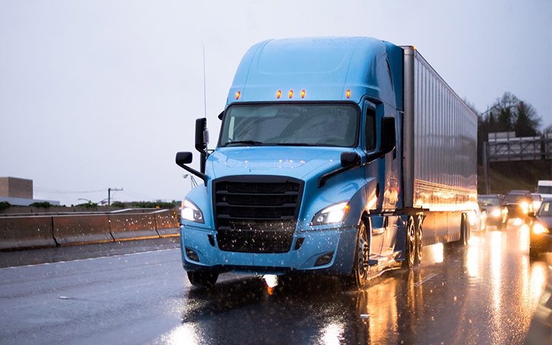 A blue semi-truck driving in the rain. 