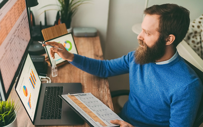 An associate compares information in a dataset to his slide decks while preparing for a work presentation.