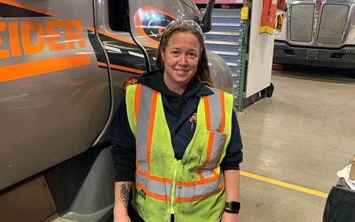 Marysa Wright, a Senior Service Advisor at Schneider who works in the Gary, Ind. shop, stands next to a Schneider tractor.