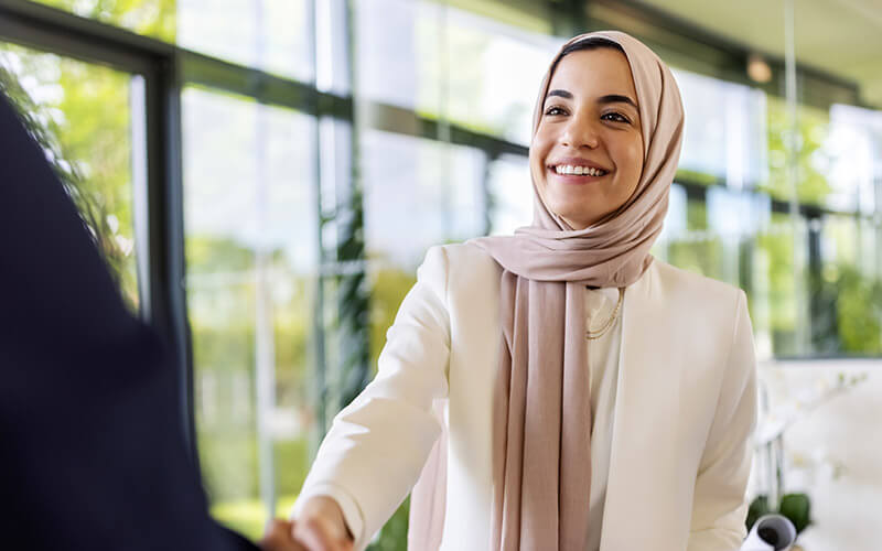 A woman, dressed for an interview, shakes someone's hand.