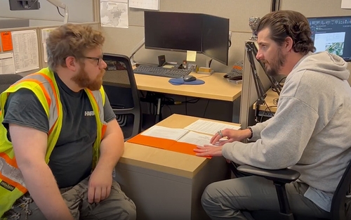 A Schneider driver and a Schneider office associate seated at a desk in an office, reviewing documents with a computer and office supplies nearby.