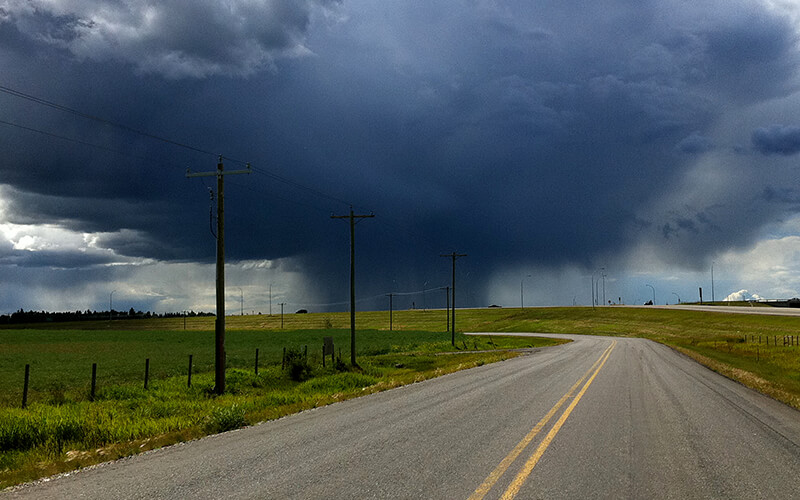 A tornado forms in the distance over a country road.