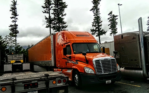 Carl Lindmark's Schneider truck parked near a trailhead where a few towering trees can be seen in the background.