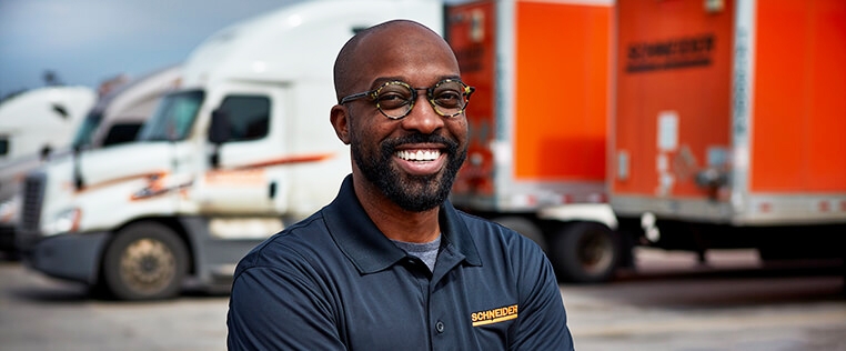 A Schneider associate poses in front of a lot of company trucks and orange trailers