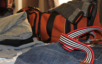 Stacks of clothes and an orange duffel bag sit on a bed.