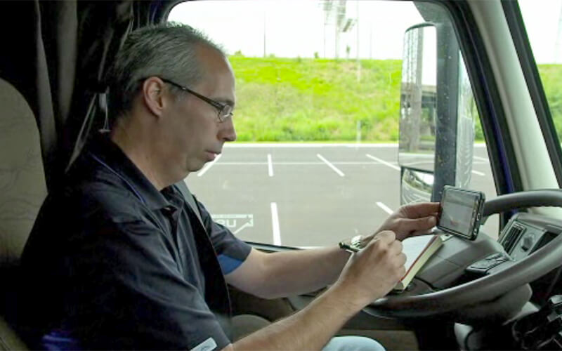 A Schneider driver writes down his load assignment on a notebook while looking on his phone.