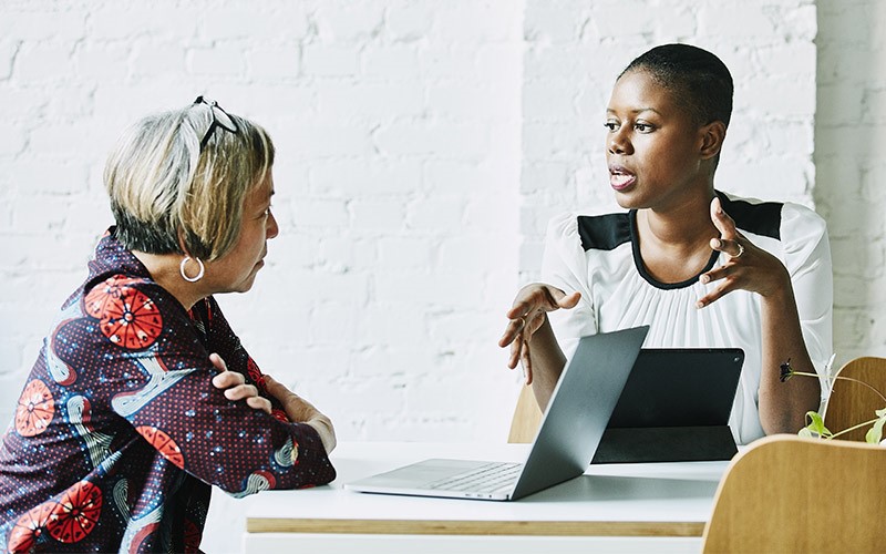 Two women sitting and talking at a desk.