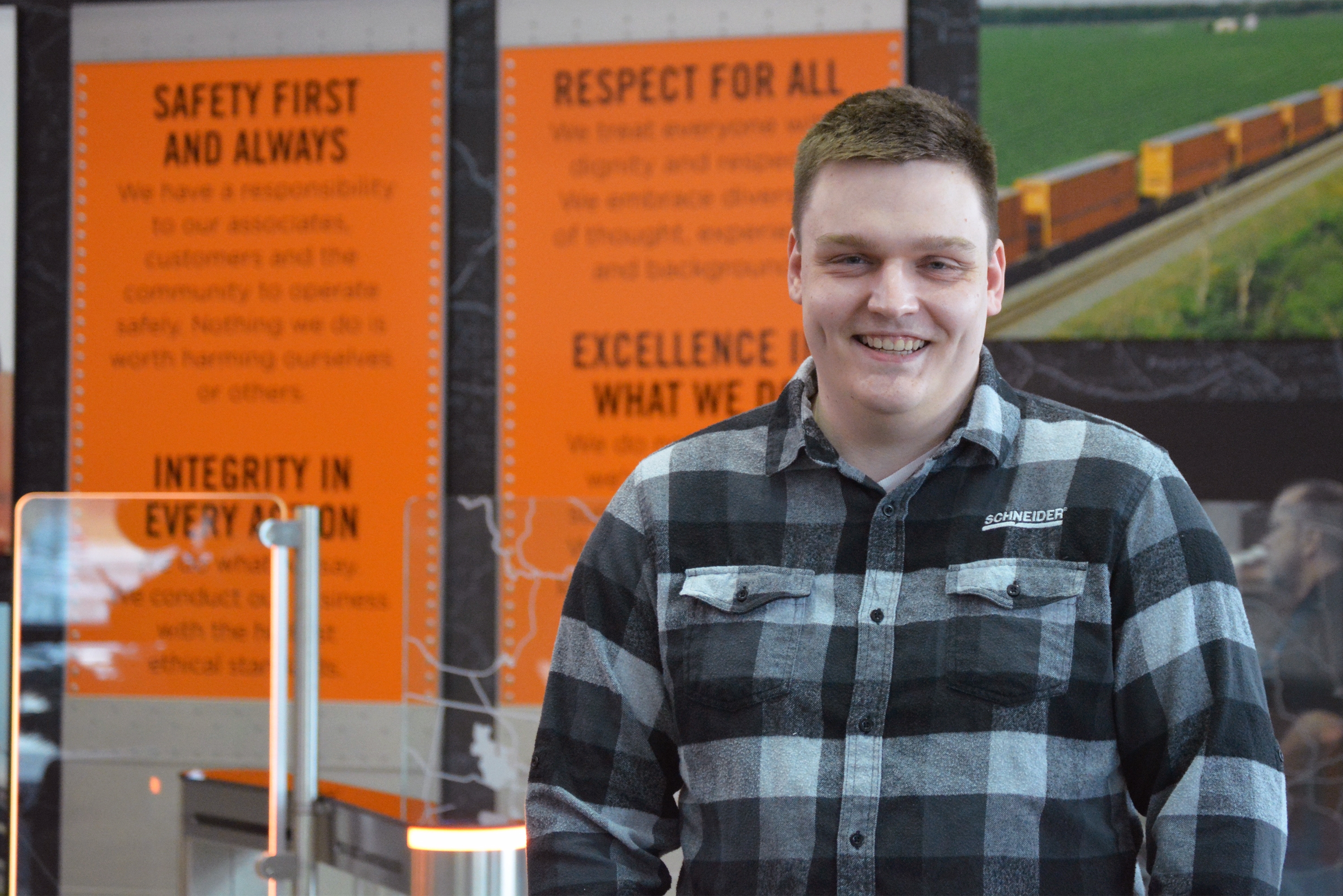 John Konicek, wearing a black, white and grey plaid shirt, poses in front of a wall in a Schneider building.