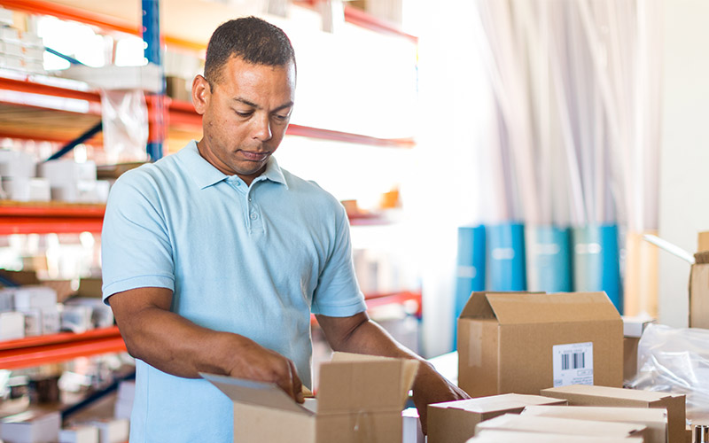 A man standing in a warehouse looking inside a cardboard box.