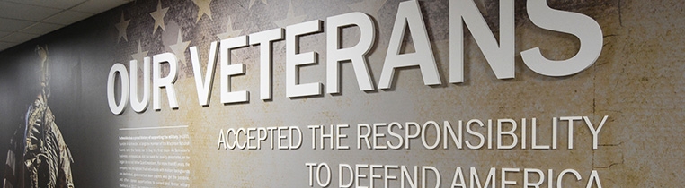 A wall display at a Schneider facility displaying the phrase "Our veterans accepted the responsibility to defend America" with a photo of a soldiers back in the distance