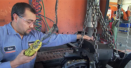 A Schneider diesel technician uses an engine lift to remove a component from the back of a semi-truck